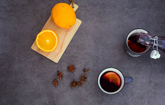 a cup of tea next to an orange on a cutting board