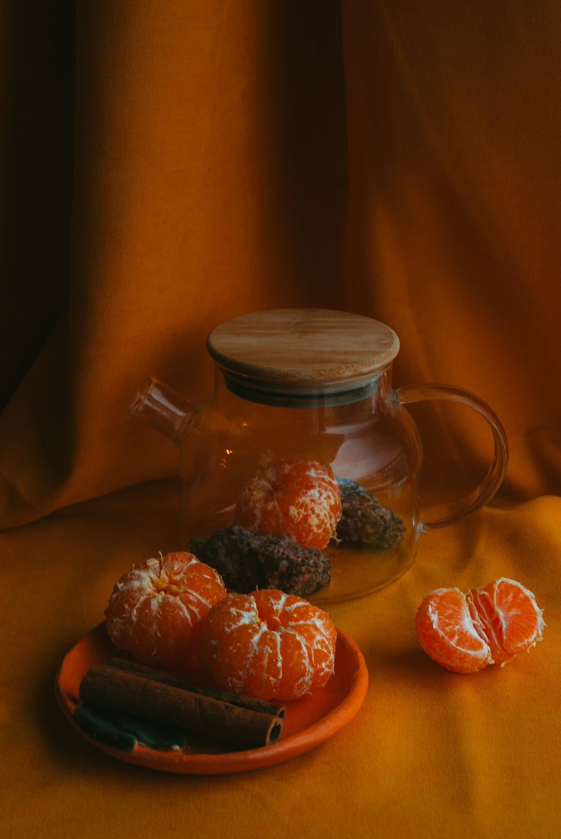 a plate of oranges and a glass teapot on a yellow cloth