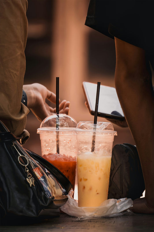 Two iced drinks with straws sit on the ground.