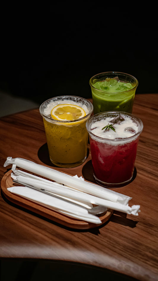 Three colorful drinks with straws on a wooden table.